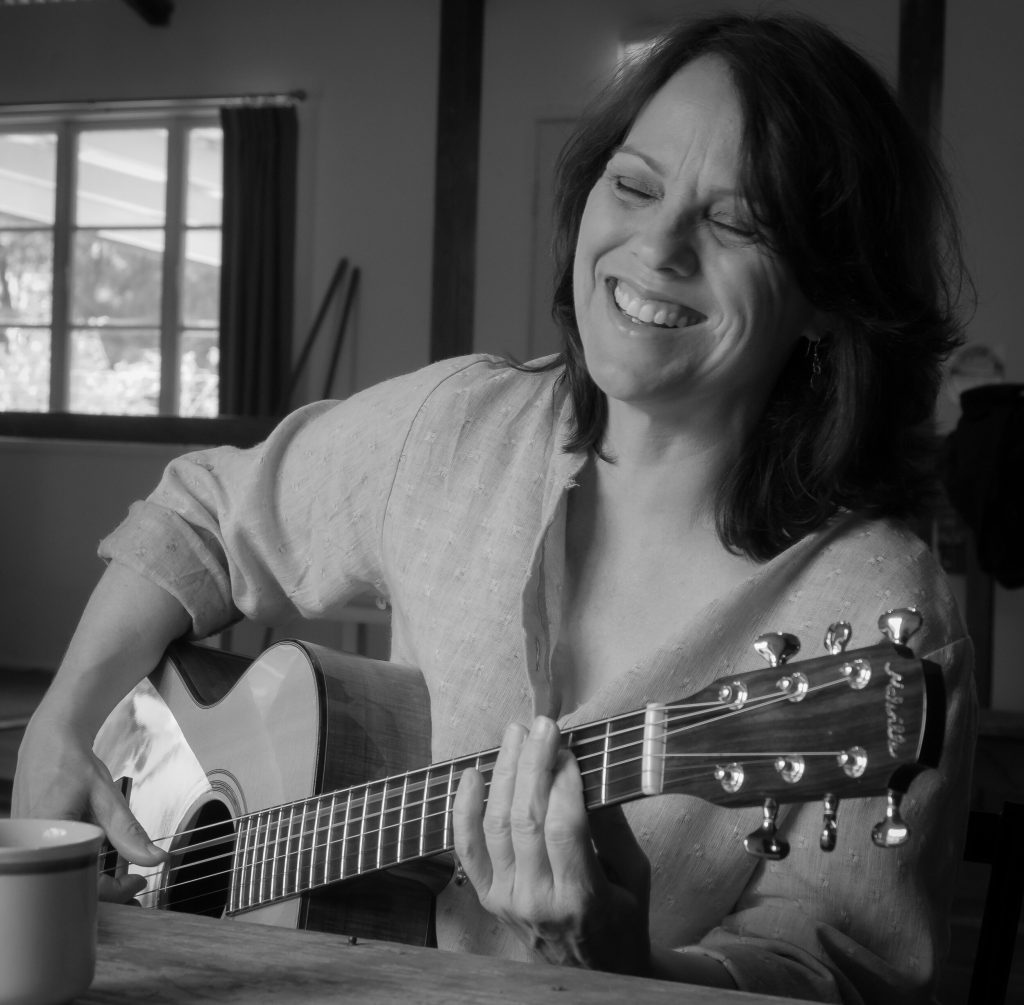 Black and white photo of Caroline playing guitar, smiling